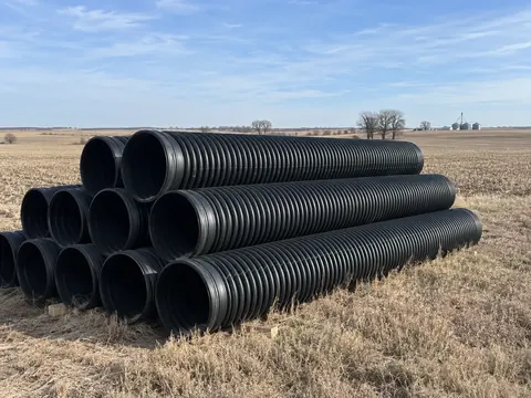 Black dual-wall HDPE culvert pipe stacked in an open field